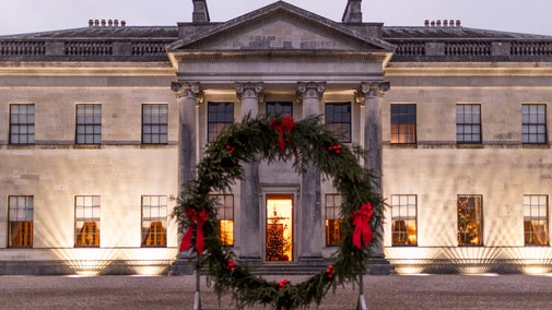 Castle Coole mansion lit up at nighttime with a wreath in front saying Merry Christmas from Castle Coole